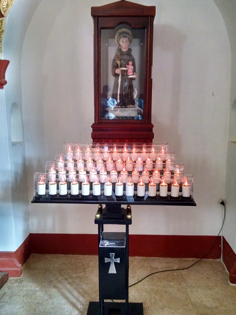 Lamparario electrónico encendido en una capilla lateral, bajo la imagen de un santo